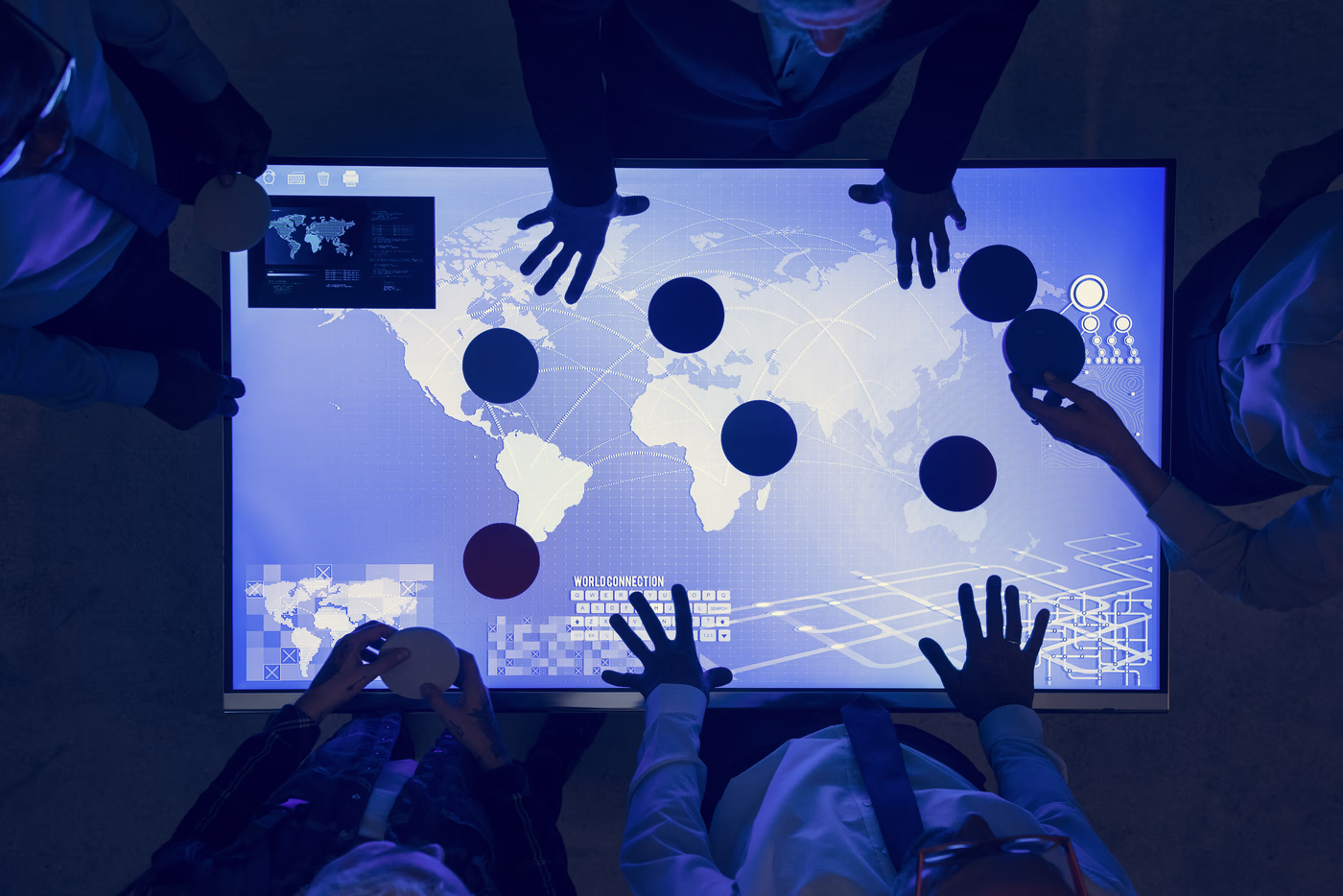 A team leaning over a lit table map, moving markers between continents.